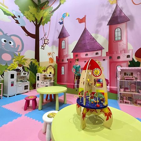 Evergreen Laurel Hotel - Taichung Eksteriør bilde The photo shows a colorful children's playroom designed with a whimsical theme. The walls are painted in bright colors and feature a cartoon-style mural of a pink castle with purple towers and a smiling cartoon elephant. The room is filled with playf