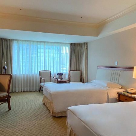 Evergreen Laurel Hotel - Taichung Eksteriør bilde The photo shows a hotel room featuring two single beds positioned near each other. There's a light-colored carpet on the floor and a large window with sheer curtains that allows natural light to fill the space. In the room, there are two chairs place