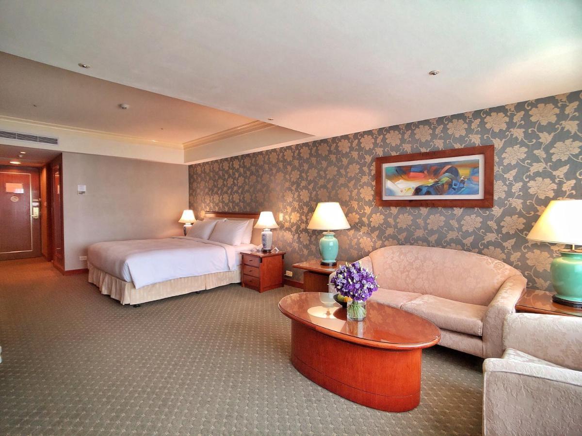 Evergreen Laurel Hotel - Taichung Eksteriør bilde The photo shows a hotel room that features a well-furnished space. It includes a large bed with a light-colored bedspread, a comfortable sofa, and armchair. There's a coffee table with a vase of flowers in the center. The room has a decorative wallpa
