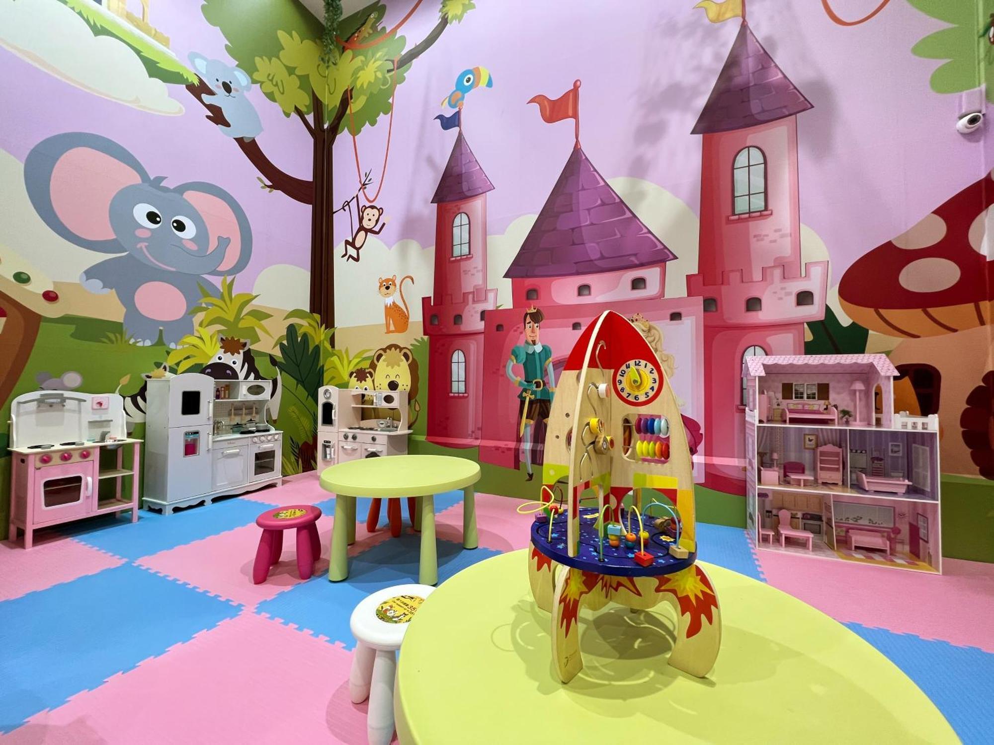 Evergreen Laurel Hotel - Taichung Eksteriør bilde The photo shows a colorful children's playroom designed with a whimsical theme. The walls are painted in bright colors and feature a cartoon-style mural of a pink castle with purple towers and a smiling cartoon elephant. The room is filled with playf