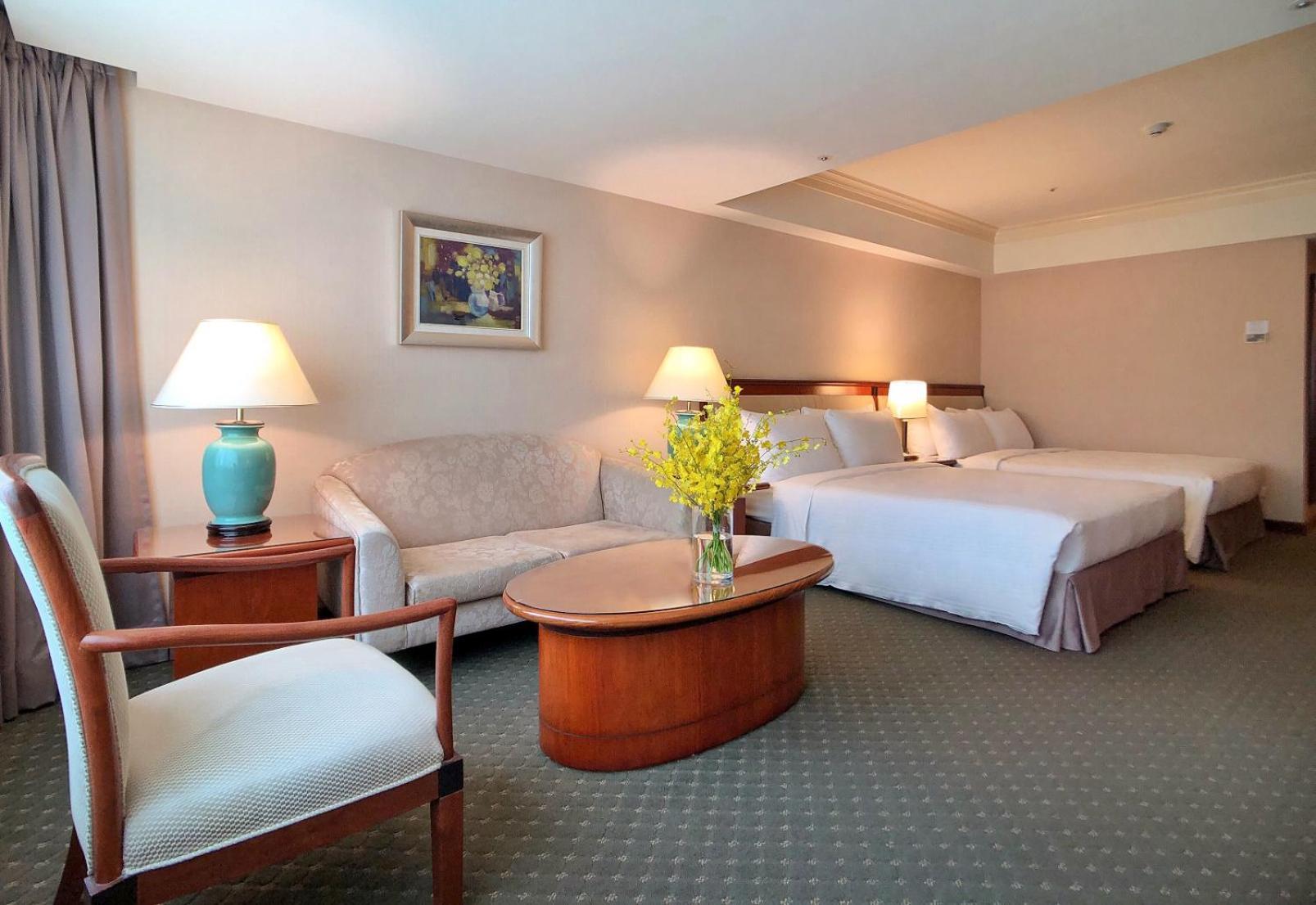 Evergreen Laurel Hotel - Taichung Eksteriør bilde The photo shows a hotel room featuring two beds, a small seating area, and a coffee table. The walls are painted in soft, neutral colors, and there is a framed piece of artwork hanging on the wall. A potted plant with yellow flowers is placed on the 