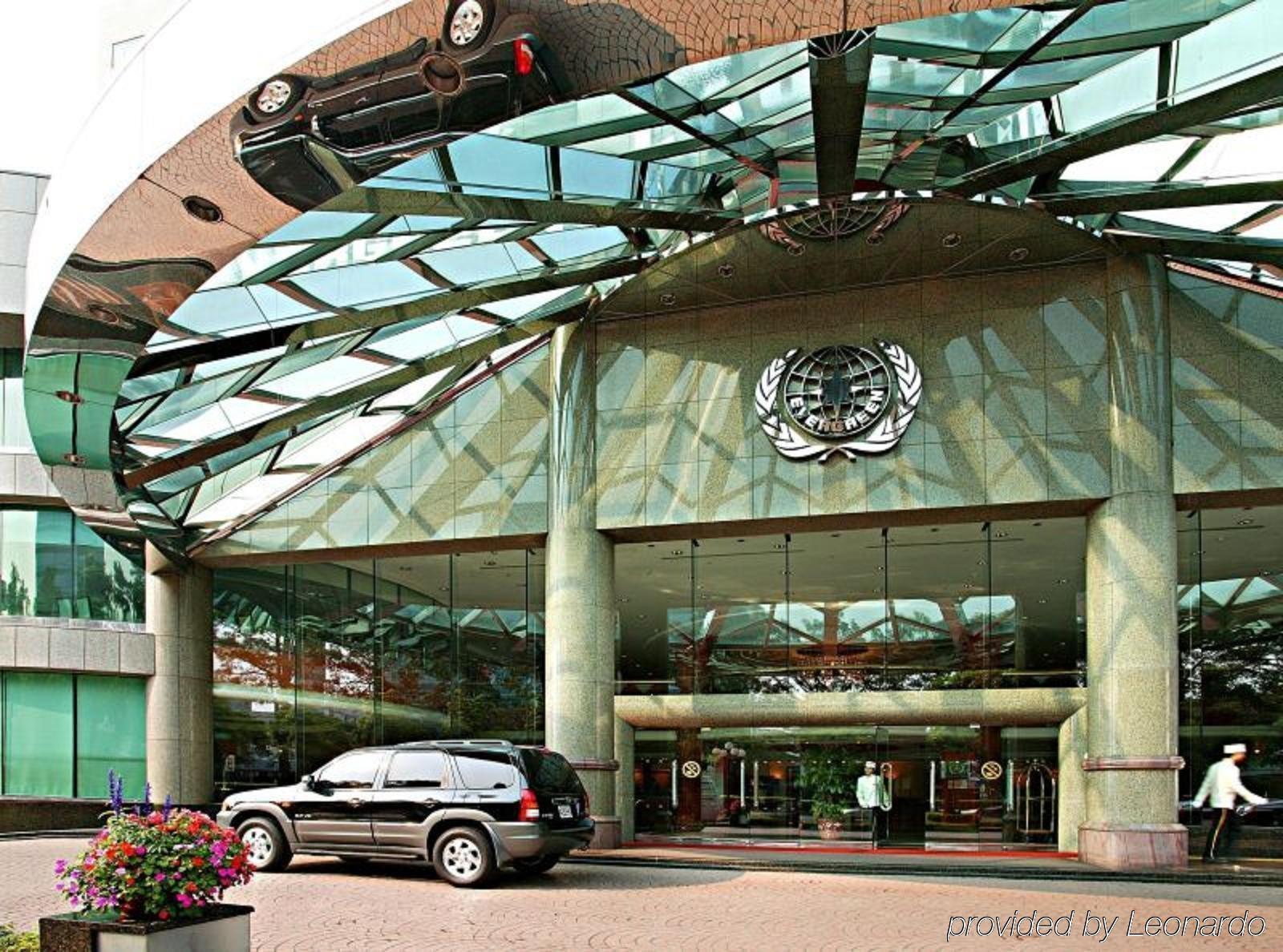 Evergreen Laurel Hotel - Taichung Eksteriør bilde The photo shows the entrance of a modern building characterized by its glass and metal architecture. The structure features a large, domed roof that reflects light, with a distinctive emblem or logo displayed prominently at the center. In front of th