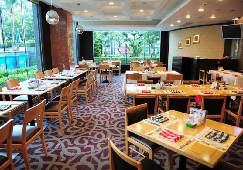 Evergreen Laurel Hotel - Taichung Eksteriør bilde The photo shows an interior of a restaurant with a spacious layout. There are several wooden tables, each set with napkins and utensils. The floor has a decorative carpet, and large windows provide a view of greenery outside. The lighting is bright, 
