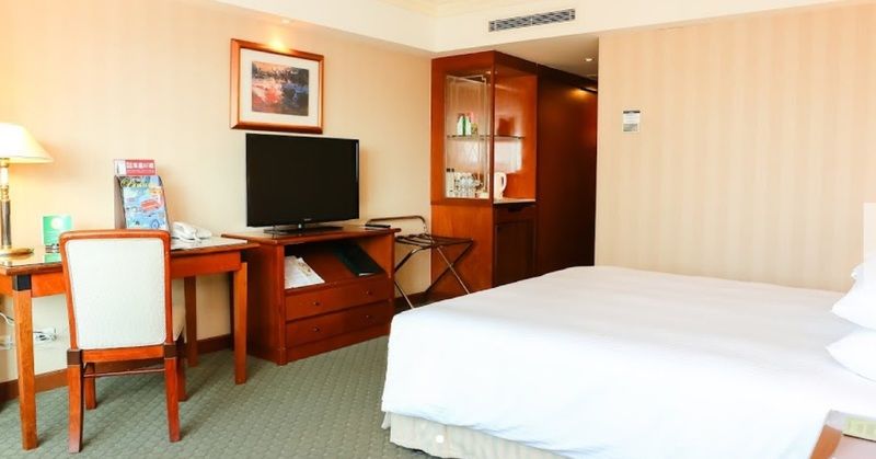 Evergreen Laurel Hotel - Taichung Eksteriør bilde The photo shows a hotel room featuring a neatly made bed with a white blanket. On one side, there is a wooden desk with a chair, and a flat-screen television is mounted nearby. An accent cabinet is visible, displaying various items. The walls are pai