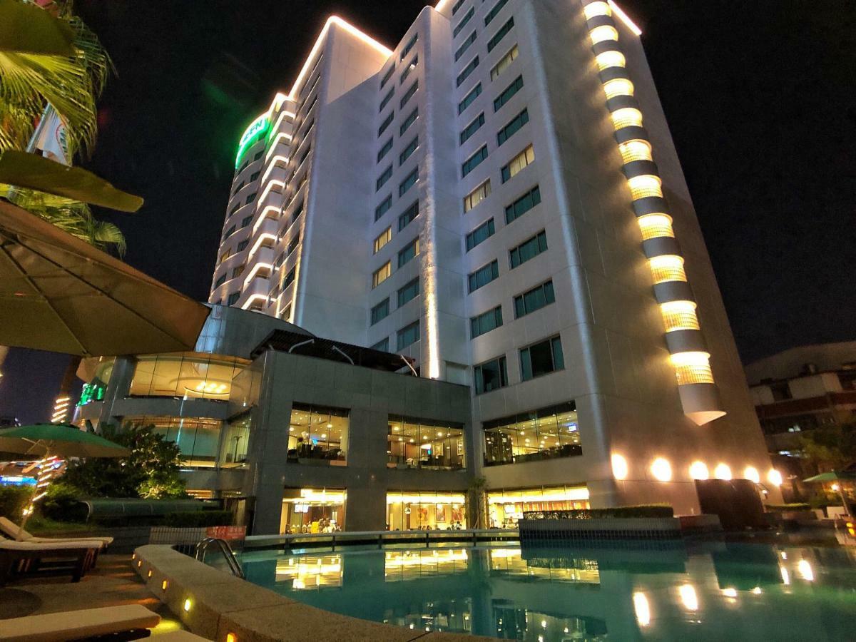 Evergreen Laurel Hotel - Taichung Eksteriør bilde The photo shows a tall hotel building at night, illuminated by lights. The architecture appears modern, with several floors and large windows. In the foreground, there is a swimming pool that reflects the lights from the building, creating a serene a