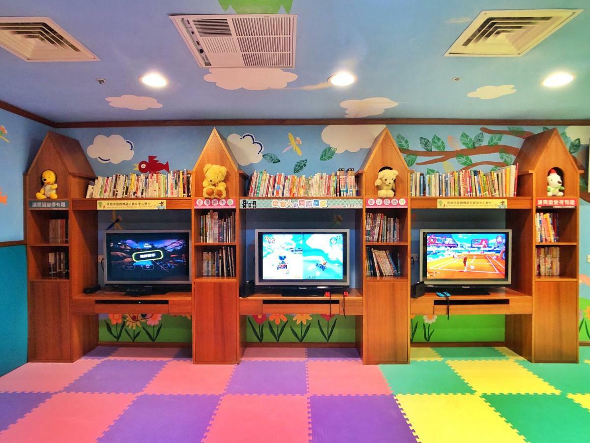 Evergreen Laurel Hotel - Taichung Eksteriør bilde The photo shows a colorful and playful room designed for children. In the center, there are three wooden gaming stations, each equipped with a television screen and surrounded by shelves filled with books. The walls are decorated with cheerful images