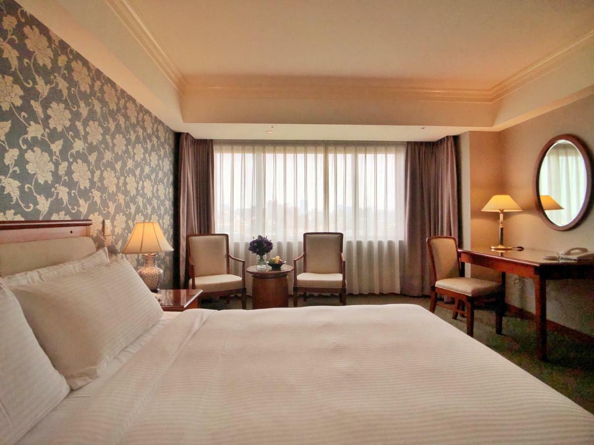 Evergreen Laurel Hotel - Taichung Eksteriør bilde The photo shows a hotel room with a comfortable and inviting design. There is a large bed with crisp white bedding on the left side of the image. To the right, there are two elegant chairs with a small round table between them, adorned with a bouquet