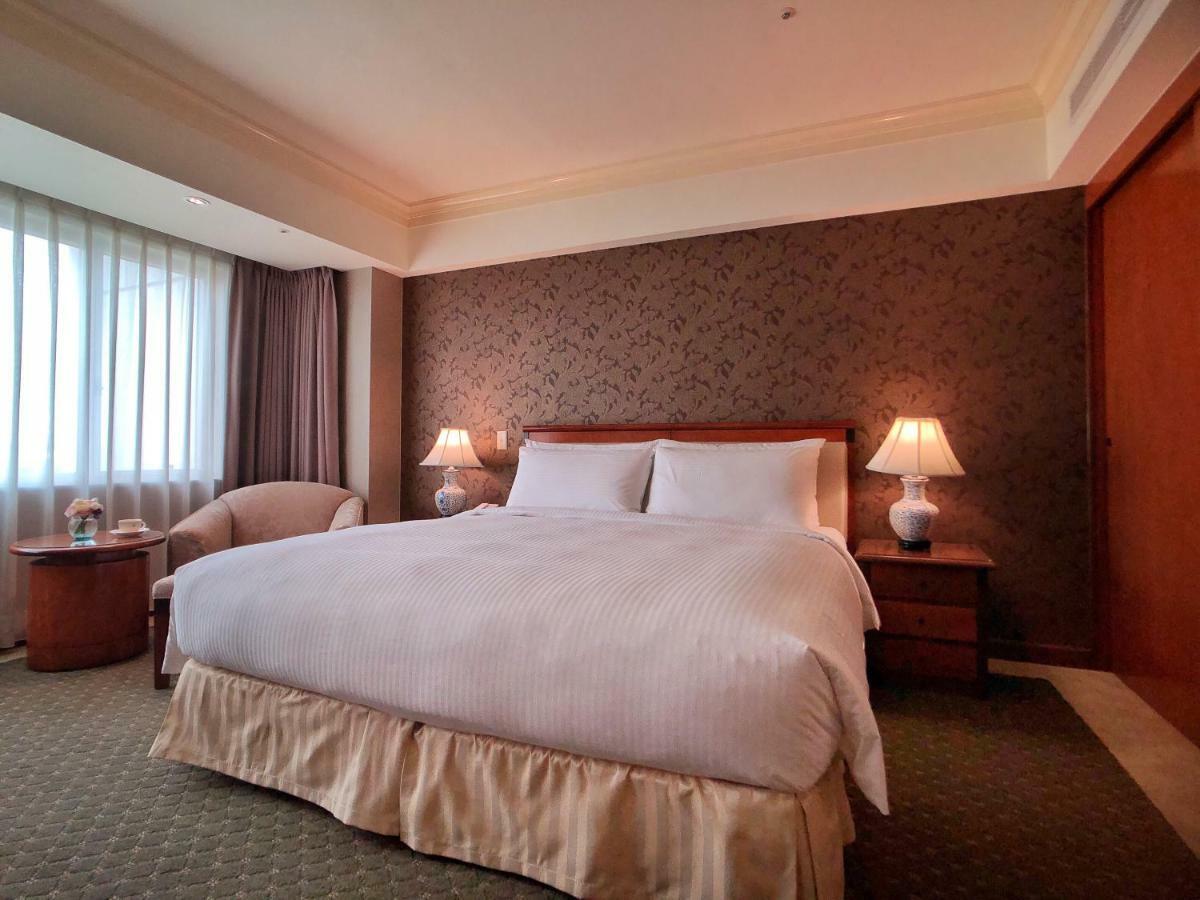 Evergreen Laurel Hotel - Taichung Eksteriør bilde The photo shows a neatly arranged hotel room featuring a large bed with white linens and a light-colored bed skirt. On either side of the bed, there are small wooden nightstands with lamps. To the left of the bed, there's a comfortable chair and a ro