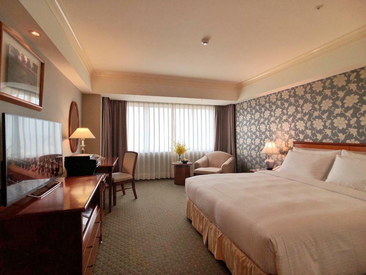 Evergreen Laurel Hotel - Taichung Eksteriør bilde The photo shows a hotel room with a spacious layout. It features a large bed with white bedding, bedside lamps, and a decorative headboard. There is a comfortable seating area with an armchair and small table. A desk is present, complete with a lamp 
