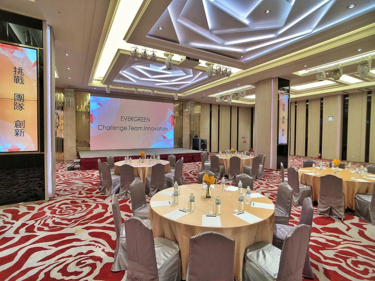Evergreen Laurel Hotel - Taichung Eksteriør bilde The photo shows a conference or event space set up for a gathering. The room features several round tables with light-colored tablecloths and chairs, each with decoration, possibly for dining or discussion. A large screen displays the text "EVERGREEN