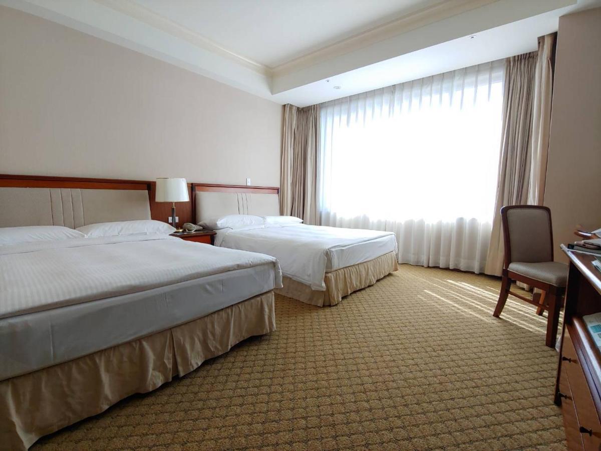 Evergreen Laurel Hotel - Taichung Eksteriør bilde The photo shows a neatly arranged hotel room featuring two beds: one double bed and one single bed. The room has beige walls and a warm color palette. Large windows with sheer curtains allow natural light to flood in, creating a bright and airy atmos