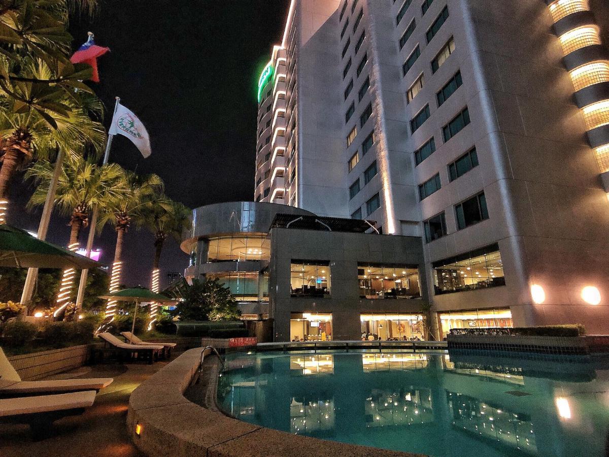 Evergreen Laurel Hotel - Taichung Eksteriør bilde The photo depicts a modern hotel or building at night, featuring a sleek facade illuminated by lights. In the foreground, there is a swimming pool that reflects the surrounding lights and palm trees. There are lounge chairs near the pool, and the atm